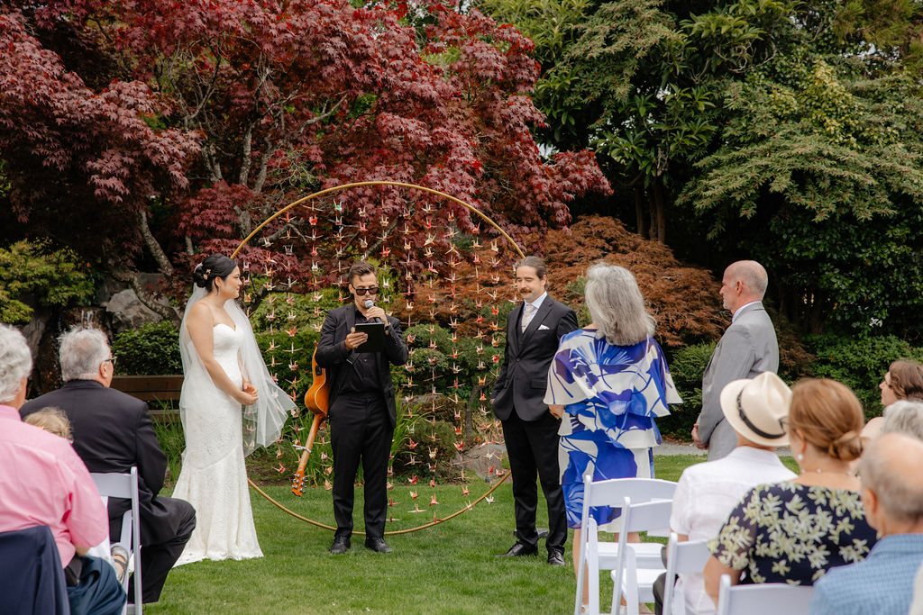 Lenny officiating between the couple at a garden ceremony